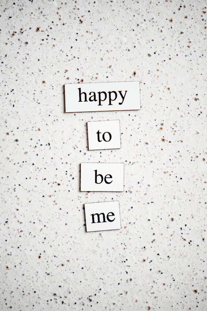 Inspirational typography message 'Happy to be me' on a speckled surface, promoting positivity.